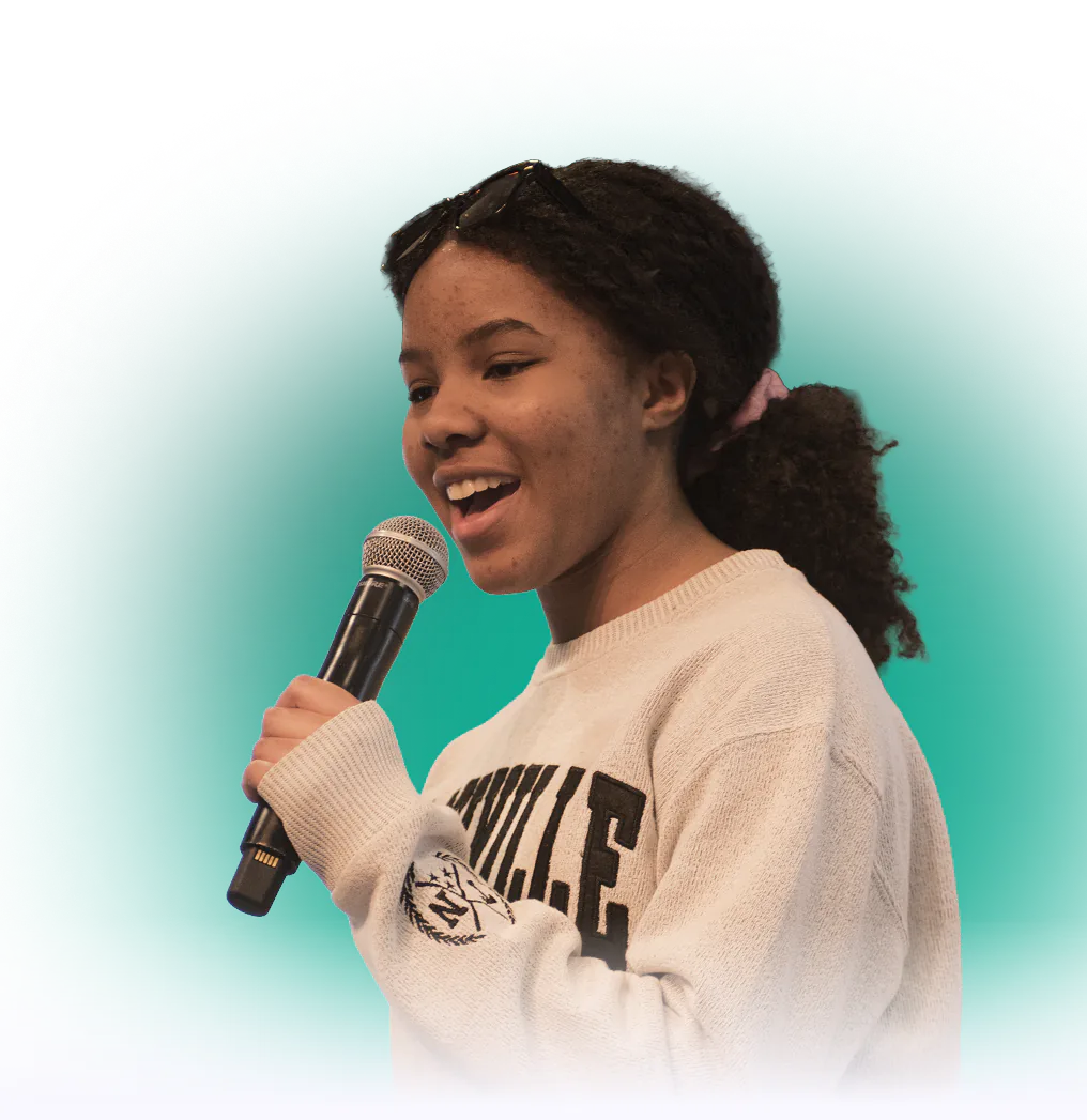 Young woman singing into a microphone while wearing a white sweatshirt.